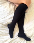 pregnant women wearing navy compression  knee-high socks on a white textured surface